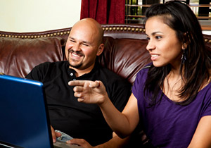 Smiling couple sitting on a couch and using a laptop computer.