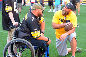 A veteran in a wheelchair talks with a player from the Pittsburgh Steelers on the turf at Heinz Field.