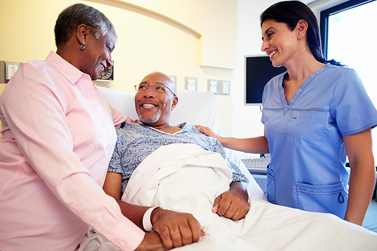 A nurse meets with a patient and family member in a hospital room.