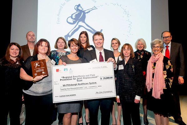 A group of employees display their award and a large check during the award presentation.