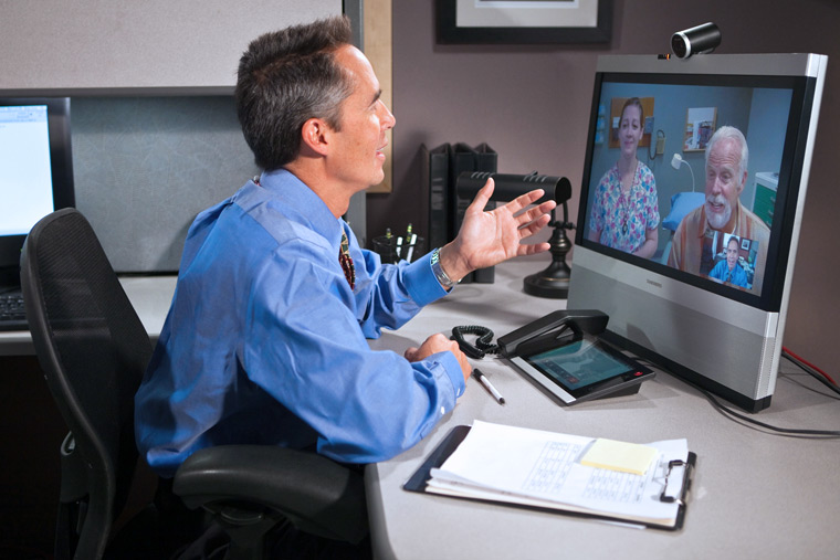 A physician consults with a veteran remotely from his office via telehealth equipment during a clinic visit.