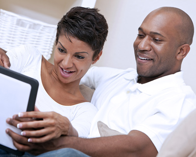 A couple sitting on a couch and looking at an iPad.