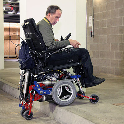 The MEBot wheelchair climbs over a curb onto a sidewalk.