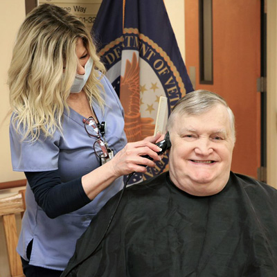 A VA staff member giving a haircut to a smiling Veteran.
