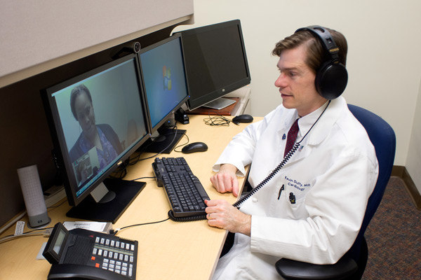 A physician interacts with a patient through video telehealth equipment.